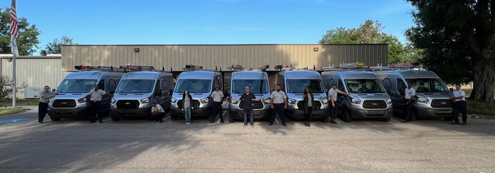 Fleet photo with 7 silver service vans and 11 staff members outside company building